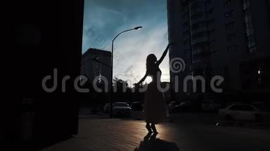 芭蕾舞演员的<strong>剪影</strong>，穿着飞行<strong>服装</strong>在户外跳舞。 苗条的女孩在城市建筑的背景下跳舞。